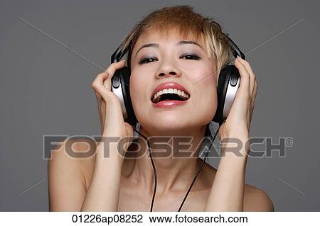 A young woman with headphones on listens to music as she looks at the camera View Large Photo Image Stock Image - A young woman with headphones on listens to music as she looks at the camera. Fotosearch