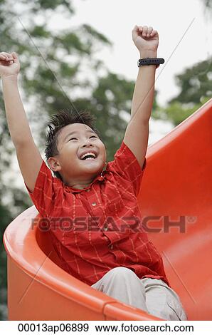 Boy coming down playground slide, arms outstretched, smiling, looking up View Large Photo Image Stock Photo - Boy coming down playground slide, arms outstretched, smiling, looking up. Fotosearch