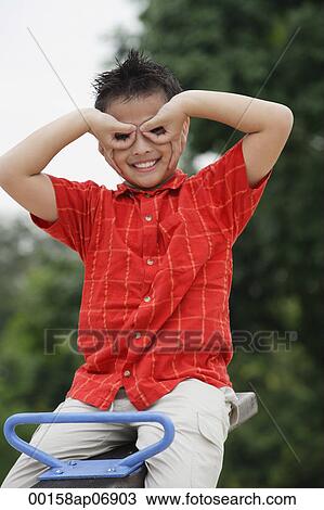 Boy sitting on See-Saw, making a mask with his fingers View Large Photo Image Stock Image - Boy sitting on See-Saw, making a mask with his fingers. Fotosearch