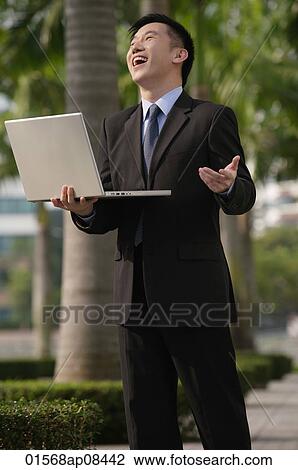 Businessman holding laptop and laughing View Large Photo Image Stock Image - Businessman holding laptop and laughing. Fotosearch