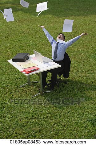 Businessman sitting at desk and throwing paper in the air View Large Photo Image Stock Image - Businessman sitting at desk and throwing paper in the air. Fotosearch