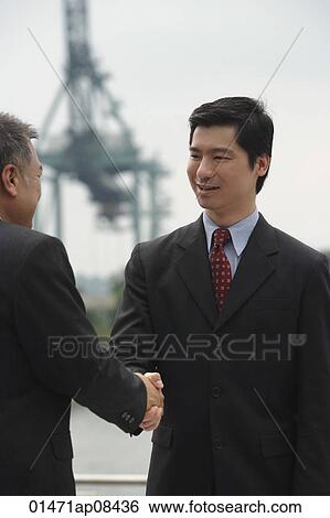 Businessmen standing face to face, shaking hands View Large Photo Image Stock Photograph - Businessmen standing face to face, shaking hands. Fotosearch