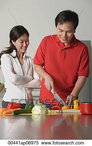 Couple in kitchen, man cutting vegetables, woman watching him View Large Photo Image Stock Photography - Couple in kitchen, man cutting vegetables, woman watching him. Fotosearch