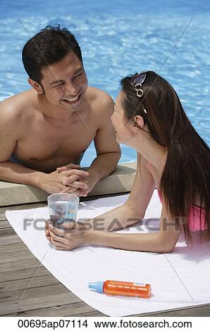 Couple looking at each other, man at the edge of swimming pool, woman lying down, holding glass of water View Large Photo Image Picture - Couple looking at each other, man at the edge of swimming pool, woman lying down, holding glass of water. Fotosearch