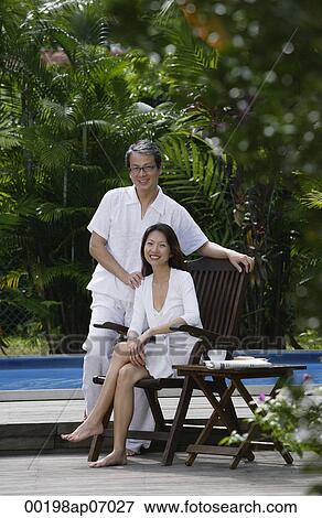 Stock Photo - Couple outdoors by swimming pool, looking at camera, portrait. Fotosearch