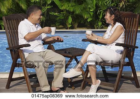 Stock Photo - Couple relaxing in deck chairs by the pool, having tea. Fotosearch