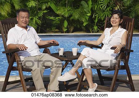 Couple relaxing in deck chairs by the pool View Large Photo Image Stock Photo - Couple relaxing in deck chairs by the pool. Fotosearch