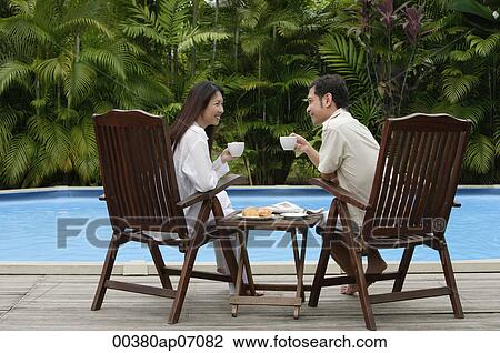 Couple sitting by swimming pool, have drinks, looking at each other View Large Photo Image Stock Image - Couple sitting by swimming pool, have drinks, looking at each other. Fotosearch