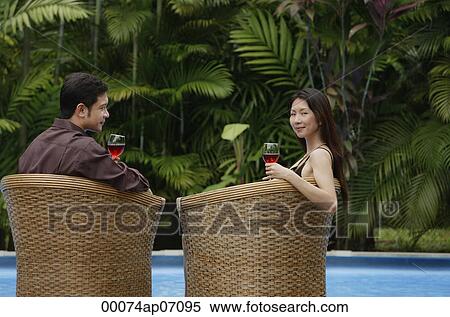 Couple sitting by swimming pool in rattan chairs, woman turning to look at camera View Large Photo Image Stock Photography - Couple sitting by swimming pool in rattan chairs, woman turning to look at camera. Fotosearch
