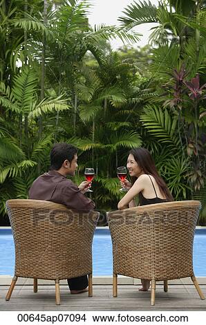 Couple sitting by swimming pool, drinking wine View Large Photo Image Picture - Couple sitting by swimming pool, drinking wine. Fotosearch