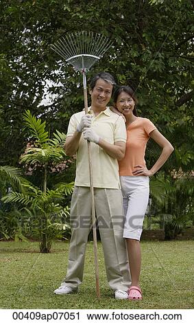 Couple standing side by side in garden, man holding garden rake View Large Photo Image Stock Image - Couple standing side by side in garden, man holding garden rake. Fotosearch