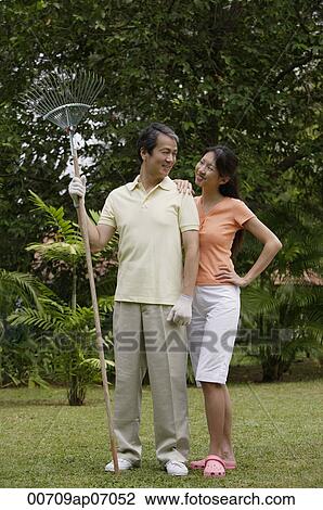 Couple standing side by side in garden, looking at each other, man holding garden rake View Large Photo Image Stock Image - Couple standing side by side in garden, looking at each other, man holding garden rake. Fotosearch