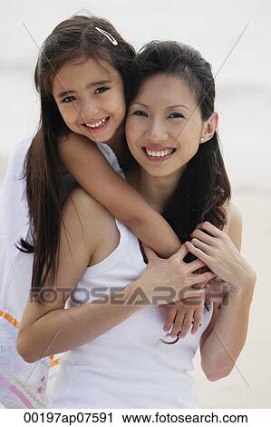 Daughter behind mother with arms over shoulders, smiling, hugging, on the beach View Large Photo Image Stock Image - Daughter behind mother with arms over shoulders, smiling, hugging, on the beach. Fotosearch