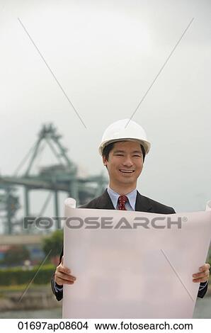 Picture - Engineer with plans and hard helmet looking at camera. Fotosearch