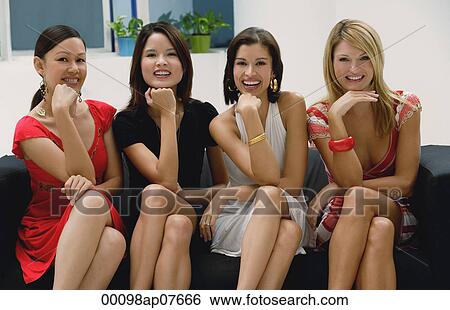 Four young women sitting on couch, legs crossed, chin resting on hand, looking at camera, smiling View Large Photo Image Stock Photograph - Four young women sitting on couch, legs crossed, chin resting on hand, looking at camera, smiling. Fotosearch