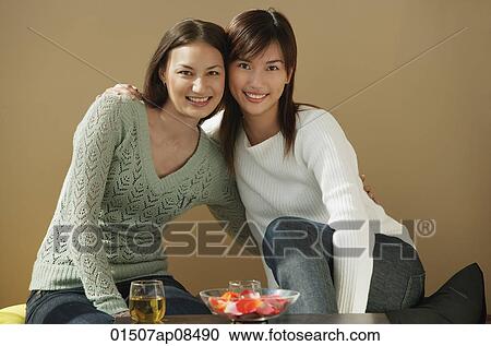 Stock Image - Friends with arms around each other smiling at camera. Fotosearch
