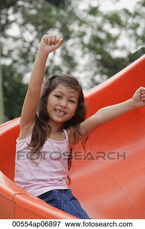 Stock Photo - Girl coming down playground slide, arms outstretched. Fotosearch