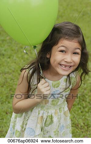 Picture - Girl holding green balloon, smiling at camera. Fotosearch
