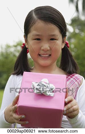 Girl holding pink wrapped gift box, smiling View Large Photo Image Stock Image - Girl holding pink wrapped gift box, smiling. Fotosearch
