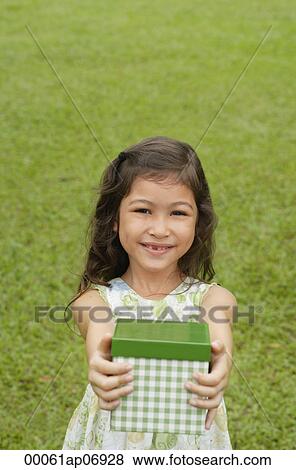 Girl standing on grass, holding gift box towards camera View Large Photo Image Stock Photo - Girl standing on grass, holding gift box towards camera. Fotosearch