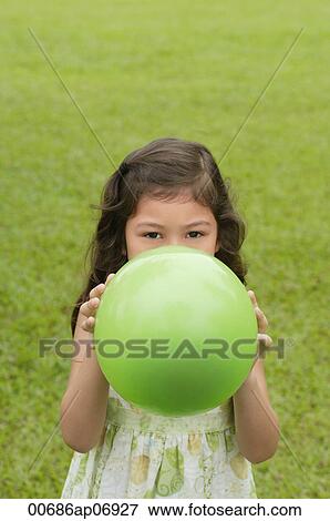 Girl standing on grass, holding green balloon over her face View Large Photo Image Stock Photo - Girl standing on grass, holding green balloon over her face. Fotosearch