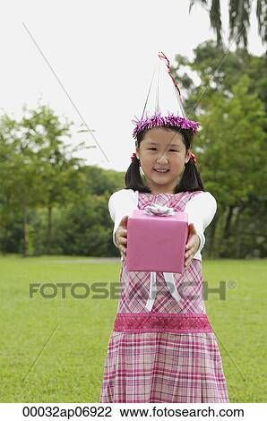 Girl with party hat holding pink gift box towards camera View Large Photo Image Stock Image - Girl with party hat holding pink gift box towards camera. Fotosearch