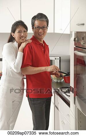 Stock Photography - Man and woman in kitchen cooking, looking at camera, smiling. Fotosearch
