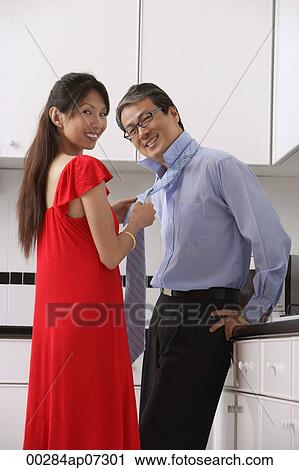Man and woman in kitchen, getting ready for night out. Woman tying mans tie, both looking at camera, smiling. View Large Photo Image Stock Image - Man and woman in kitchen, getting ready for night out. Woman tying mans tie, both looking at camera, smiling.. Fotosearch