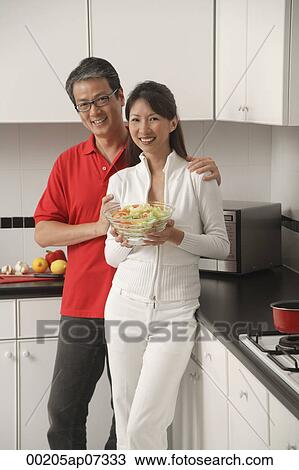 Man and woman in kitchen holding salad bowl and looking at camera smiling View Large Photo Image Stock Image - Man and woman in kitchen holding salad bowl and looking at camera smiling. Fotosearch