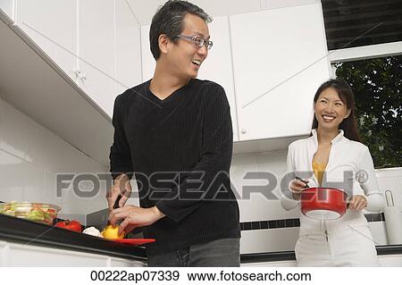 Stock Photo - Man and woman in kitchen preparing a meal, cooking, smiling at each other. Fotosearch