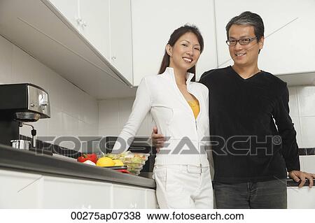 Man and woman in kitchen preparing a meal, smiling at camera View Large Photo Image Stock Photo - Man and woman in kitchen preparing a meal, smiling at camera. Fotosearch