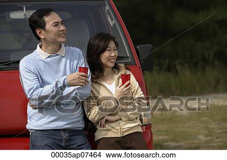 Man and woman leaning against red van, drinks in hand, camping, outdoors View Large Photo Image Picture - Man and woman leaning against red van, drinks in hand, camping, outdoors. Fotosearch