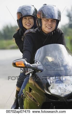 Man and woman riding motorcycle, wearing helmets, looking at camera View Large Photo Image Stock Photography - Man and woman riding motorcycle, wearing helmets, looking at camera. Fotosearch