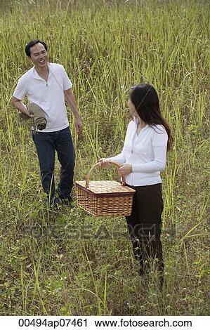 Stock Image - Man and woman walking outdoors, carrying picnic basket and blanket. Fotosearch