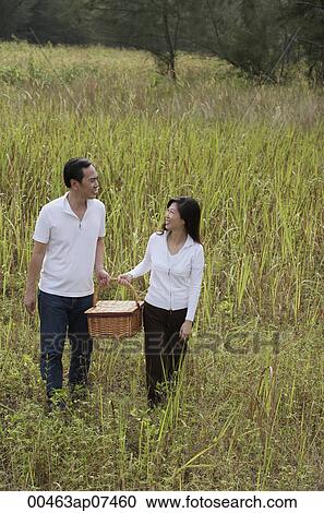 Stock Image - Man and woman walking through nature carrying picnic basket. Fotosearch