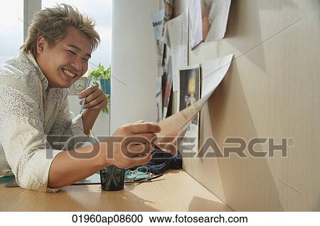 Man at desk smiling while looking at paper View Large Photo Image Stock Image - Man at desk smiling while looking at paper. Fotosearch