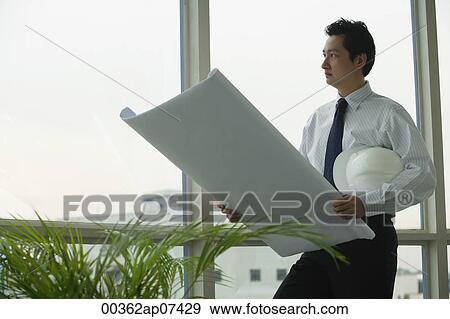man holding blue prints and construction hat looking out window View Large Photo Image Stock Photo - man holding blue prints and construction hat looking out window. Fotosearch