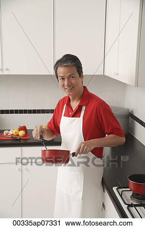 Man in kitchen cooking with sauce pan, looking at camera, wearing apron View Large Photo Image Stock Image - Man in kitchen cooking with sauce pan, looking at camera, wearing apron. Fotosearch