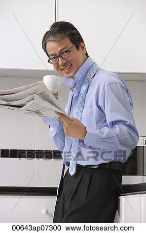 Man in kitchen getting ready for work, drinking coffee and reading newspaper, smiling at camera with tie loose around neck View Large Photo Image Stock Image - Man in kitchen getting ready for work, drinking coffee and reading newspaper, smiling at camera with tie loose around neck. Fotosearch