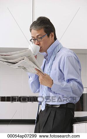 Man in kitchen getting ready for work, drinking coffee and reading newspaper, tie loose around neck View Large Photo Image Stock Photo - Man in kitchen getting ready for work, drinking coffee and reading newspaper, tie loose around neck. Fotosearch