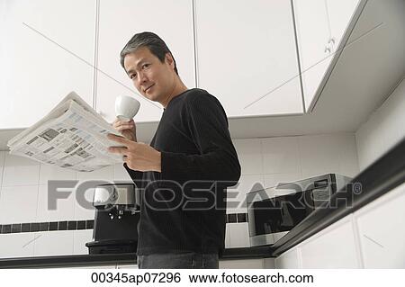 Man in kitchen, holding coffee cup and newspaper and looking at camera View Large Photo Image Stock Photograph - Man in kitchen, holding coffee cup and newspaper and looking at camera. Fotosearch