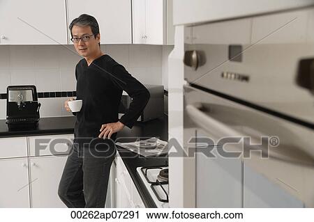 Man in kitchen holding coffee cup, looking at camera View Large Photo Image Stock Image - Man in kitchen holding coffee cup, looking at camera. Fotosearch
