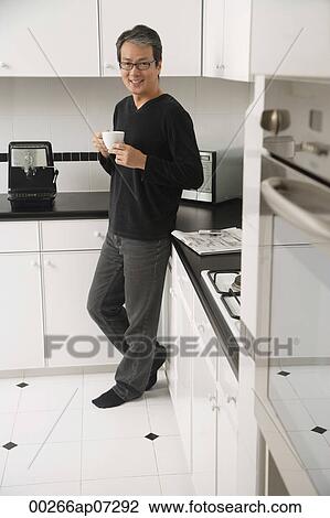 Man in kitchen, leaning on counter, holding coffee cup and smiling at camera View Large Photo Image Stock Image - Man in kitchen, leaning on counter, holding coffee cup and smiling at camera. Fotosearch