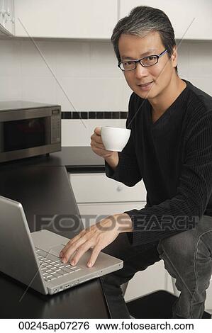 Man in kitchen with laptop / computer, looking at camera, sitting on stool, smiling and holding coffee cup. View Large Photo Image Stock Photograph - Man in kitchen with laptop / computer, looking at camera, sitting on stool, smiling and holding coffee cup.. Fotosearch