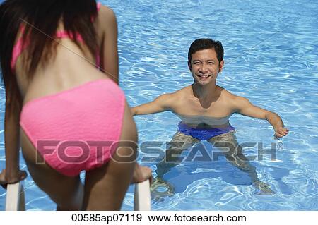 Man in swimming pool, smiling at woman standing in front of him View Large Photo Image Stock Photo - Man in swimming pool, smiling at woman standing in front of him. Fotosearch
