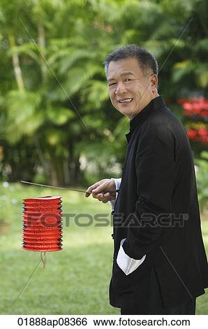 Man in traditional clothing, standing in park holding Chinese lantern View Large Photo Image Stock Photograph - Man in traditional clothing, standing in park holding Chinese lantern. Fotosearch
