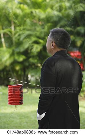 Man in traditional clothing, standing in park holding Chinese lantern View Large Photo Image Stock Photography - Man in traditional clothing, standing in park holding Chinese lantern. Fotosearch