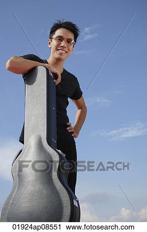 Stock Image - Man leaning against guitar case. Fotosearch