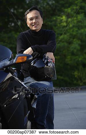 Man leaning on motorcycle, holding helmet, smiling at camera View Large Photo Image Stock Photo - Man leaning on motorcycle, holding helmet, smiling at camera. Fotosearch