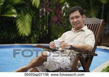 Man sitting by swimming pool, holding a cup of coffee View Large Photo Image Stock Photograph - Man sitting by swimming pool, holding a cup of coffee. Fotosearch